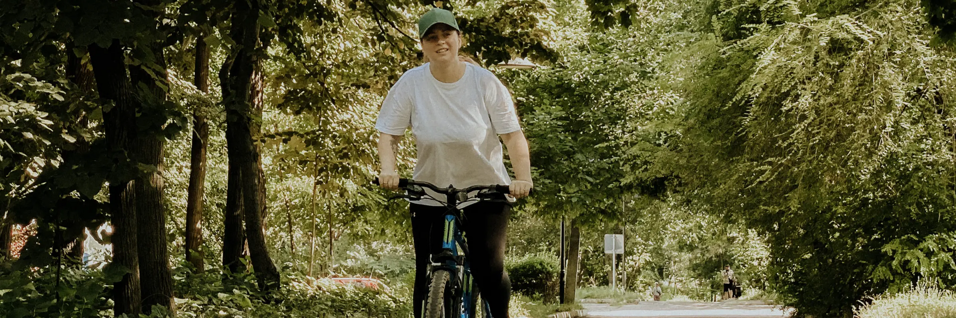 Otyła młoda kobieta z czapką na głowie jadąca na rowerze po parku