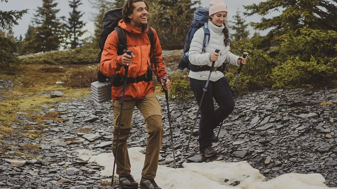 Kobieta i mężczyzna z plecakami wędrujący po górach z kijkami trekkingowymi