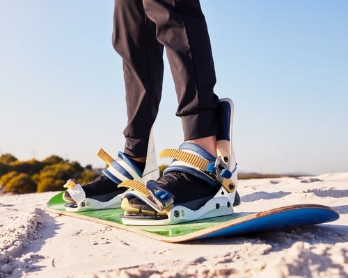 Mężczyzna ćwiczący sandboarding stojoący na desce na pustyni