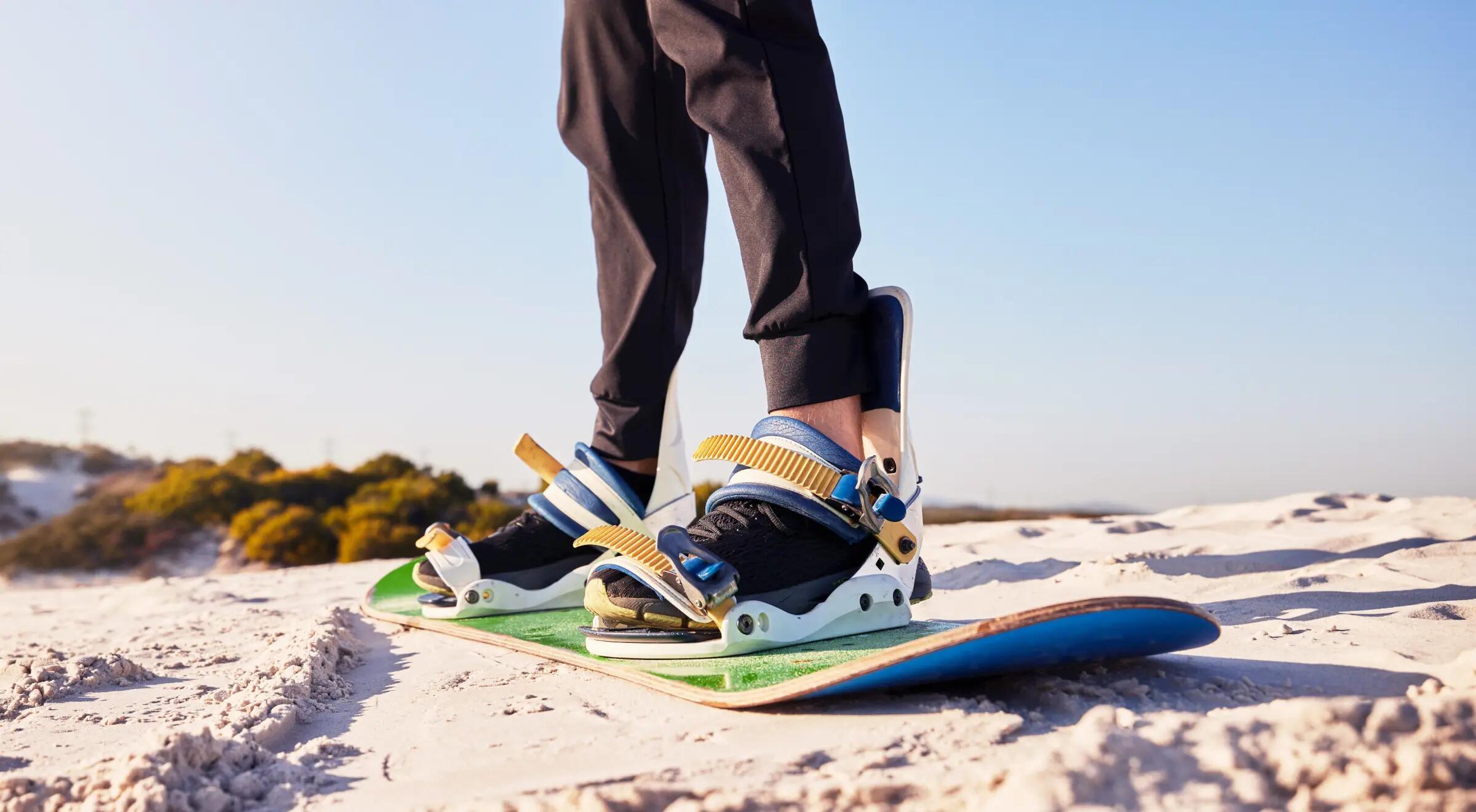 Mężczyzna ćwiczący sandboarding stojoący na desce na pustyni