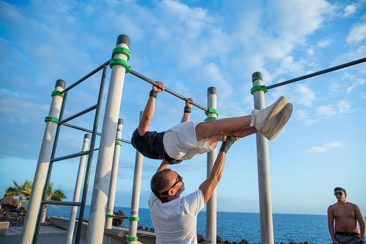 Mężczyzna pomagający chłopakowi wykonać front lever na drabinkach