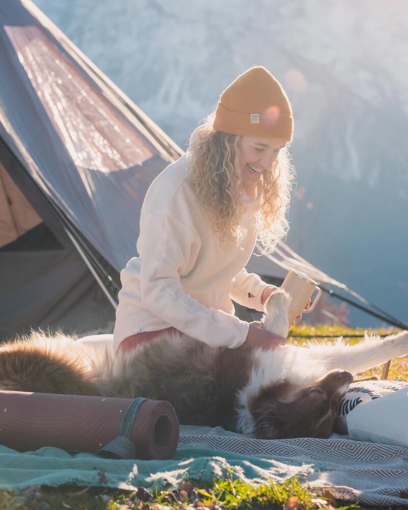 Eine Frau sitzt vor Ihrem Zelt auf dem Boden und macht Quatsch mit ihrem Hund