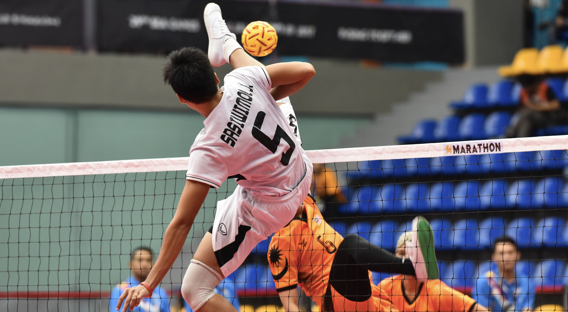 Chłopak przebijający piłkę nogą przez siatkę grający w sepak takraw