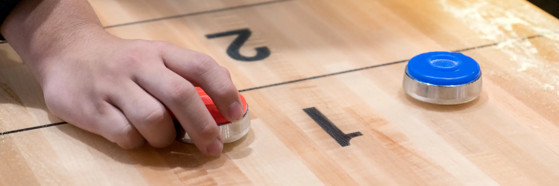 Ręka przesuwająca krążek po stołowym boisku od shuffleboard