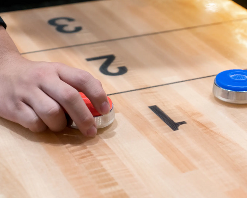 Ręka przesuwająca krążek po stołowym boisku od shuffleboard