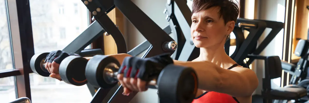 Kobieta w odzieży sportowej ćwicząca wznosy hantlami przodem