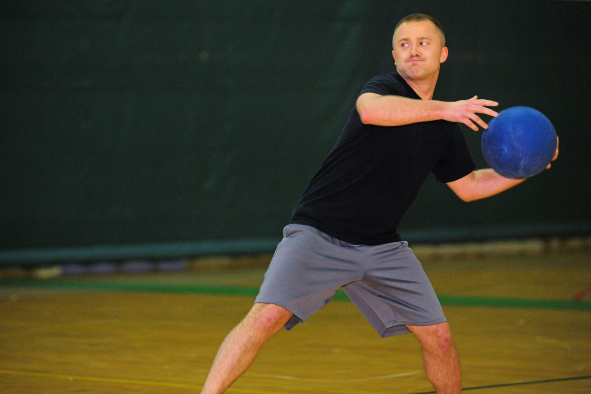 Mężczyzna w stroju sportowym stojący na sali trzymajacy piłkę w rękach