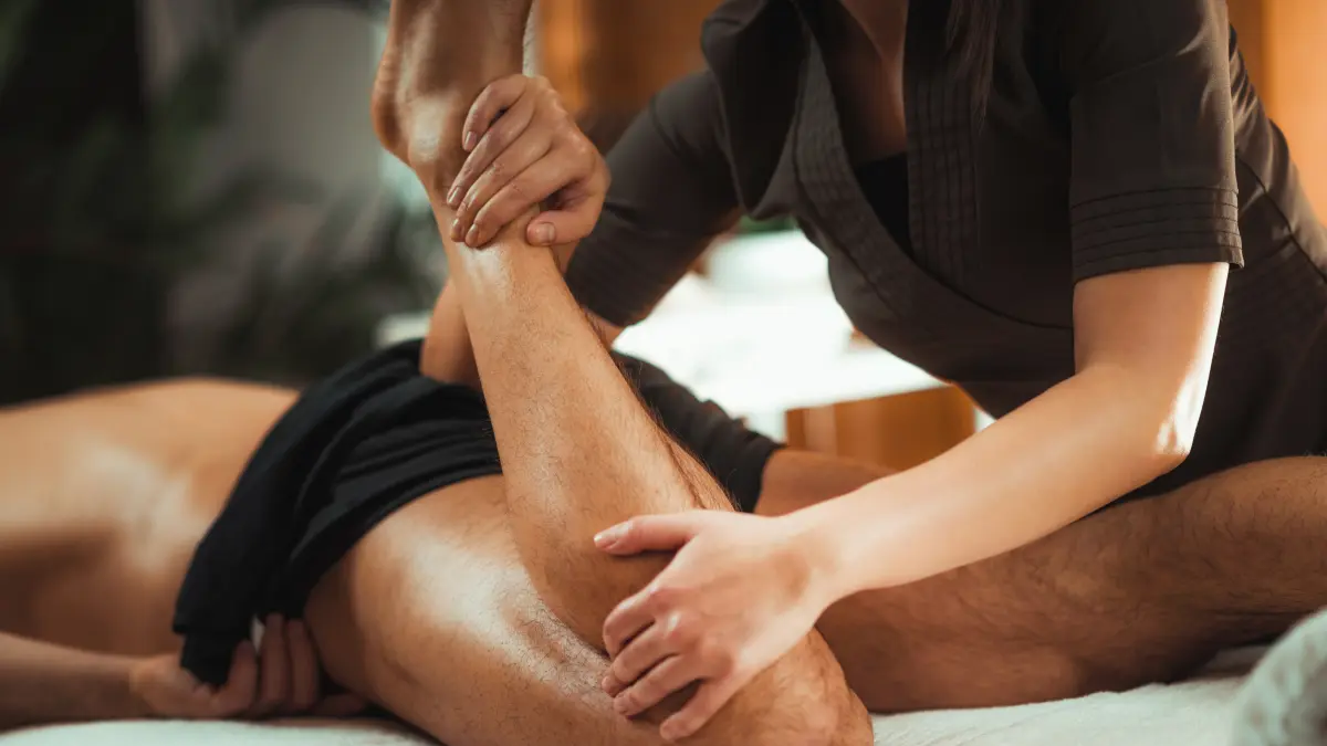 Masażystka zginający nogę leżącemu mężczyźnie podczas masażu sportowego