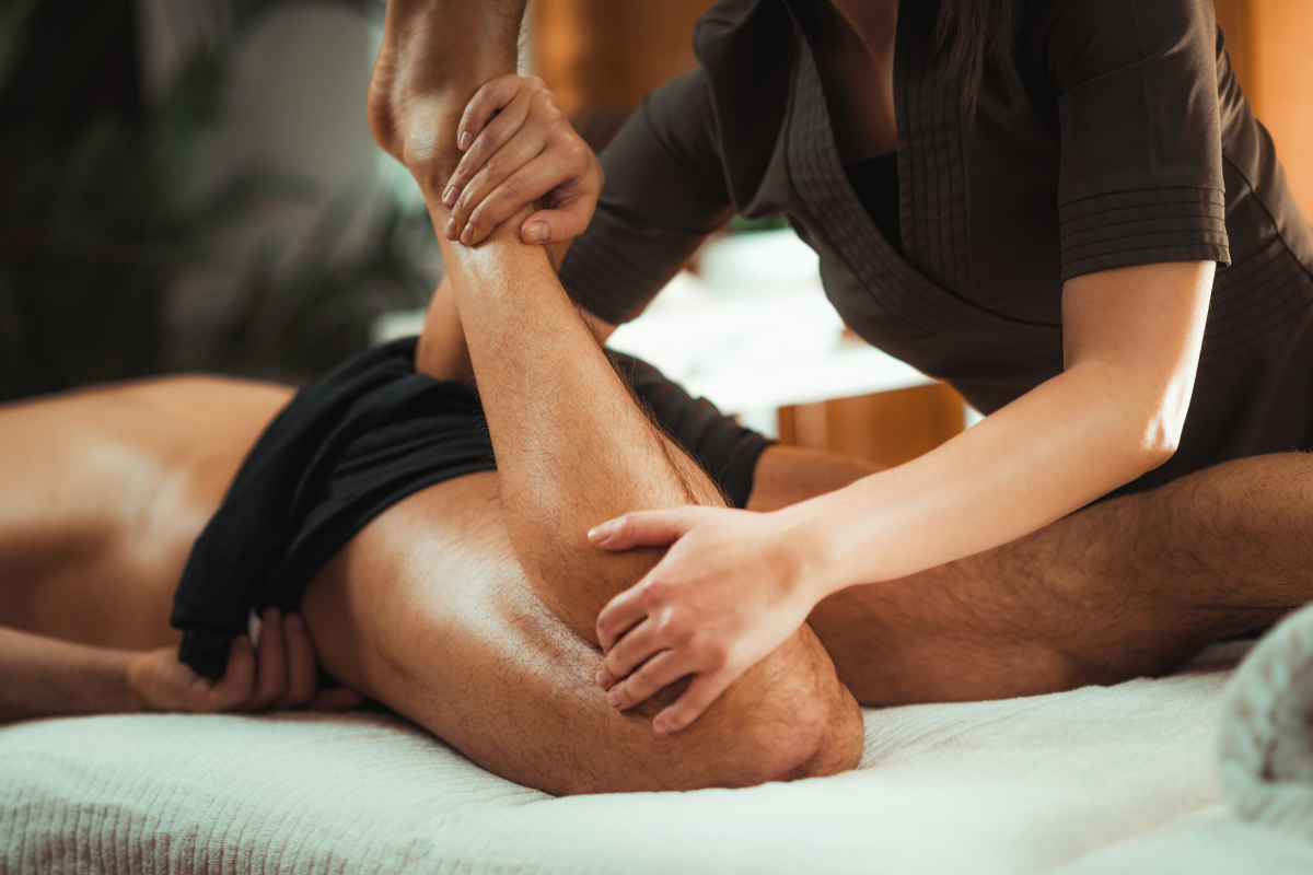 Masażystka zginający nogę leżącemu mężczyźnie podczas masażu sportowego