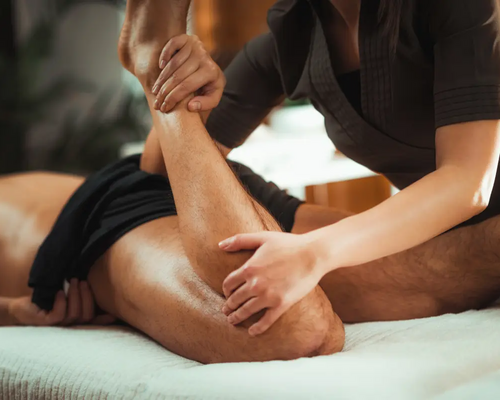 Masażystka zginający nogę leżącemu mężczyźnie podczas masażu sportowego