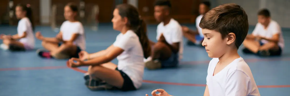 Dzieci w odzieży sportowej medytujące na sali gimnastycznej