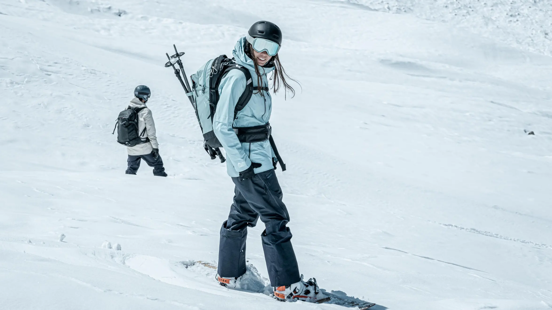 Kobieta w odzieży zimowej z plecakiem na plecach stojąca na desce snowboardowej