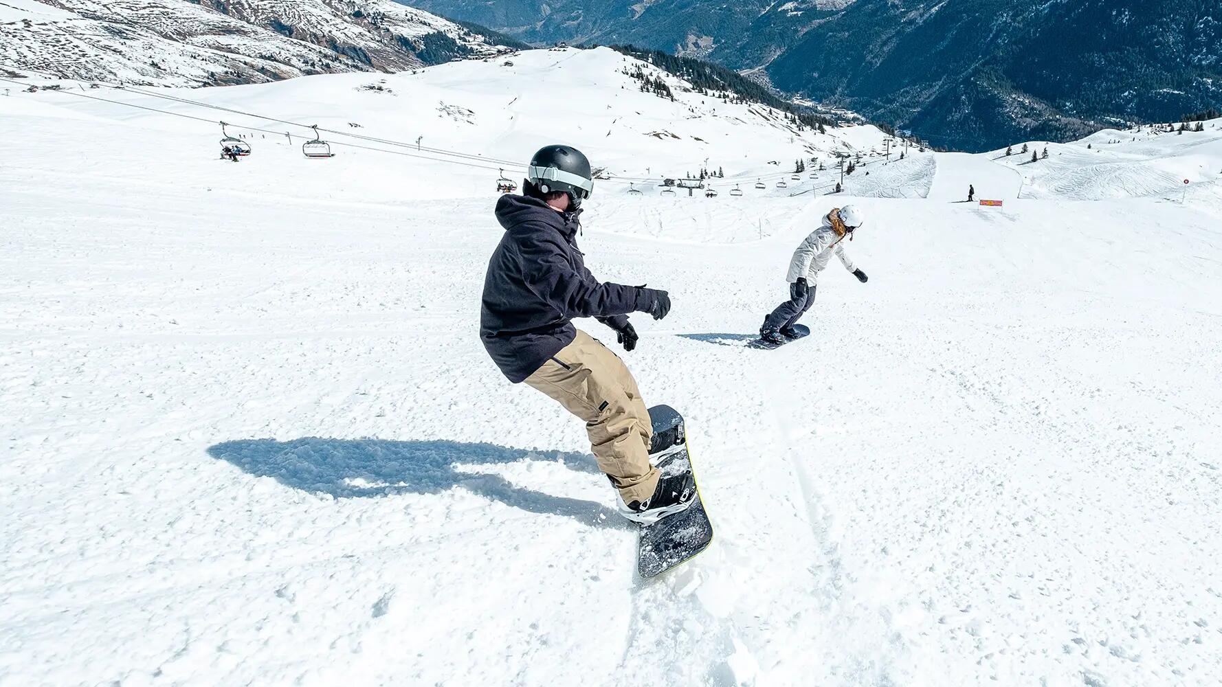 Para w kaskach i w goglach jeżdżąca na snowboardzie po stoku