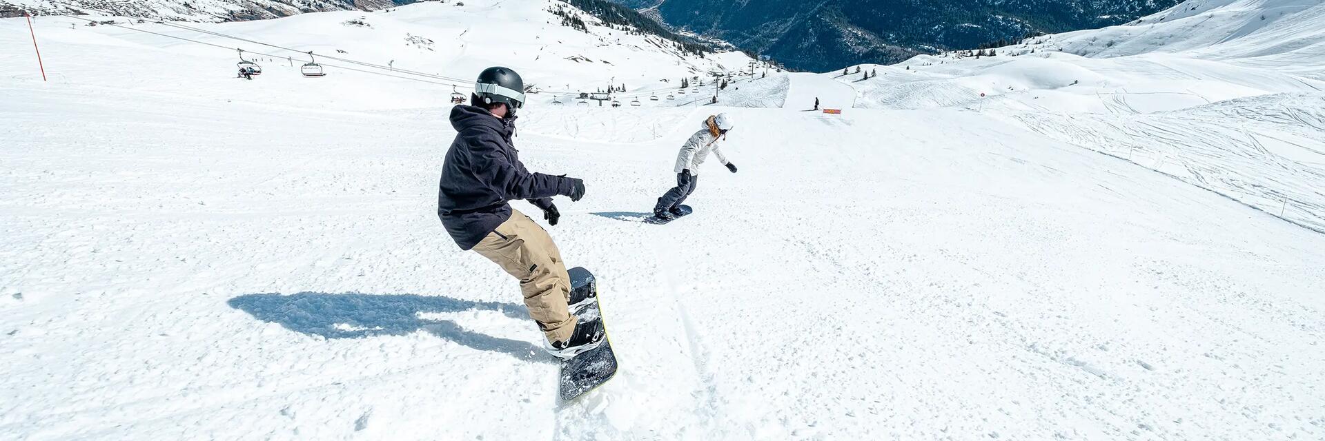 Kobieta i mężczyzna w kaskach i w goglach jeżdżący na snowboardzie na stoku
