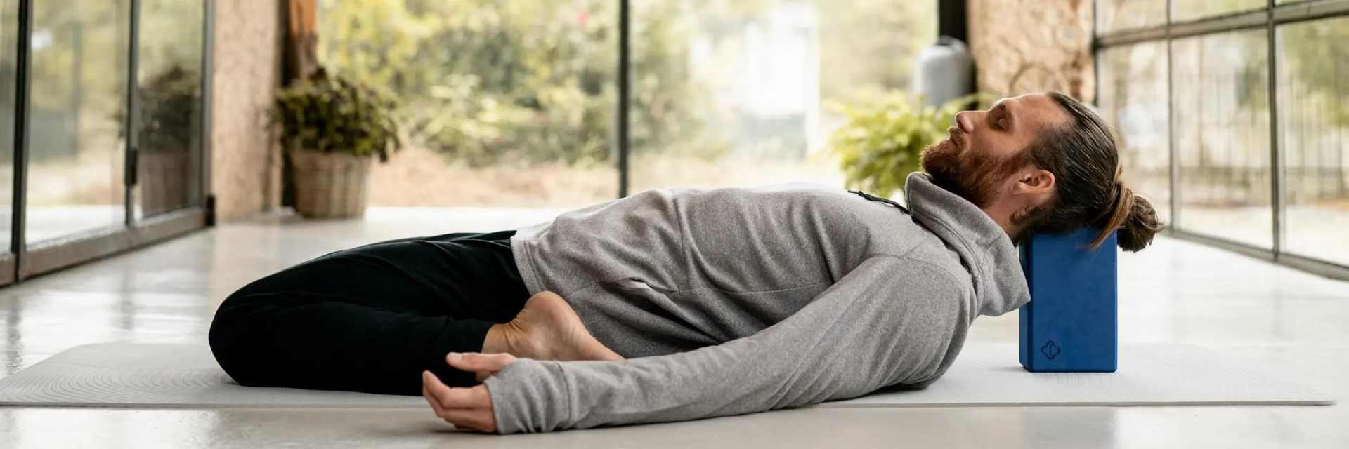 Mężczyzna ćwiczący matsyasana z klockiem pod głową w jodze