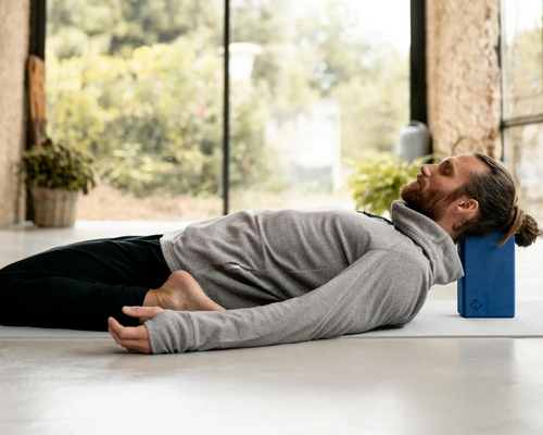 Mężczyzna ćwiczący matsyasana z klockiem pod głową w jodze