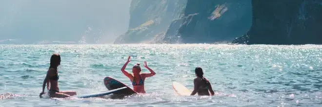 Trzy kobiety z deskami surfingowymi w wodzie