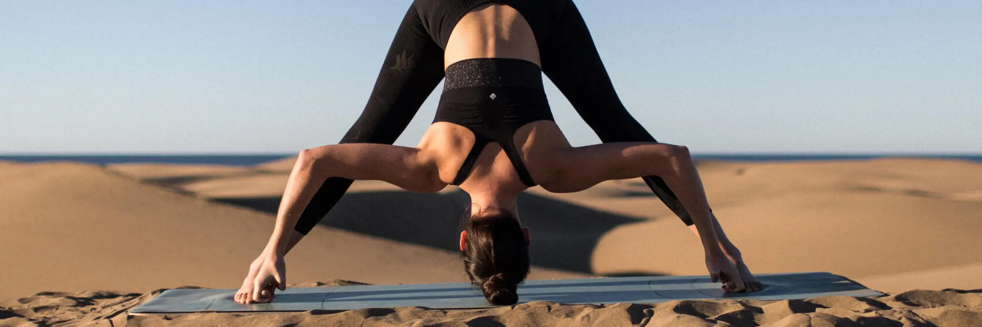 Kobieta ćwicząca na plaży na macie pozycję prasarita padottanasana