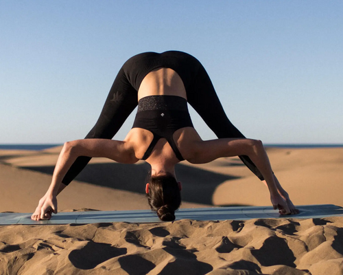 Kobieta ćwicząca na plaży na macie pozycję prasarita padottanasana