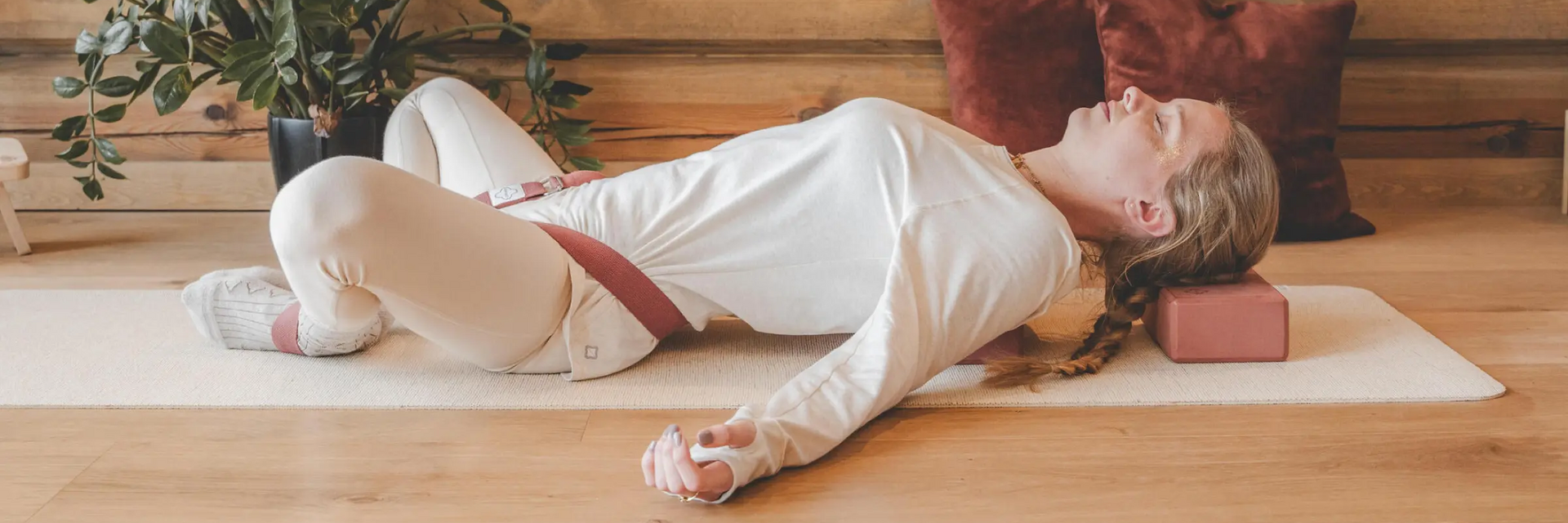 Kobieta leżąca z zamkniętymi oczami na macie z klockiem pod głową w pozycji supta baddha konasana w jodze
