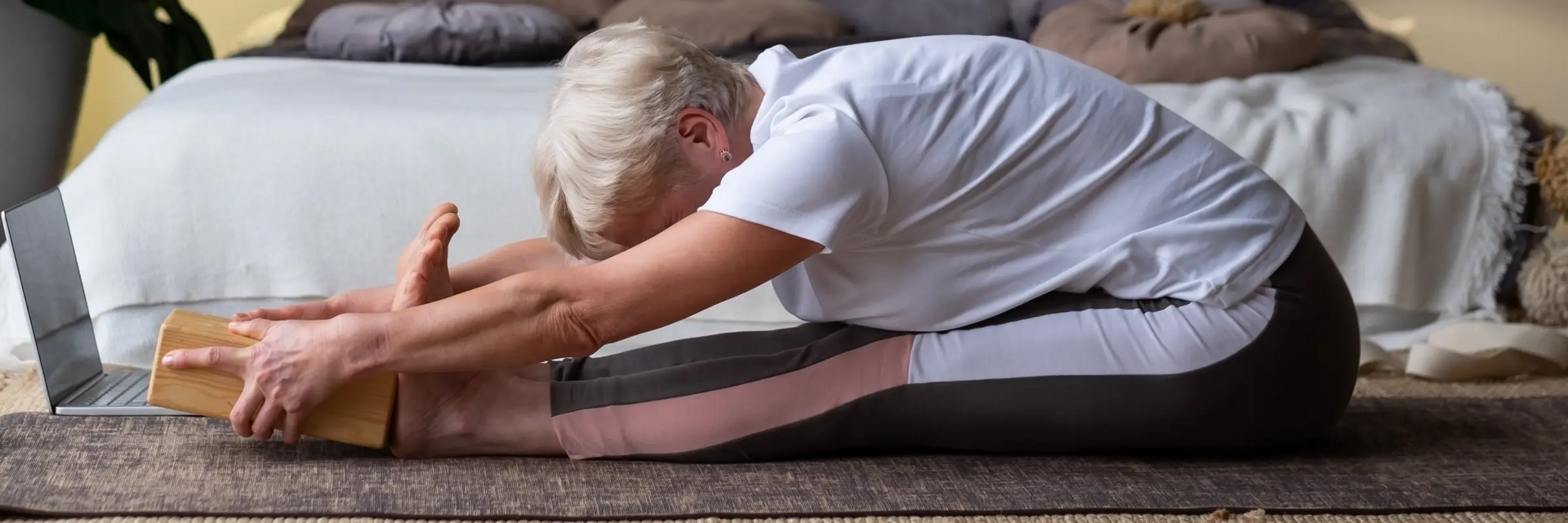 Dojrzała kobieta ćwicząca z klockiem na macie pozycję paschimottanasana