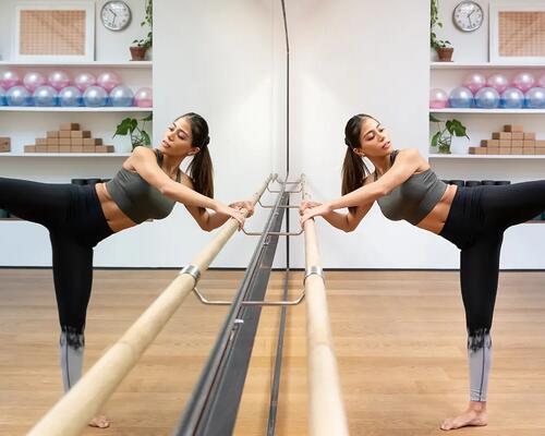 Kobieta w stroju sportowym ćwicząca barre pilates przed lustrem trzymając się drążka