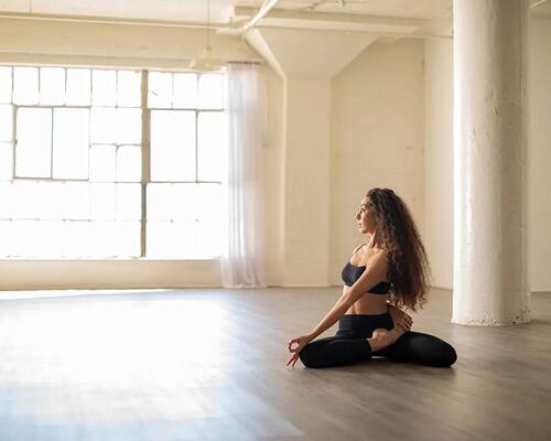 Kobieta ćwicząca na podłodze pozycję bharadvajasana w jodze na sali