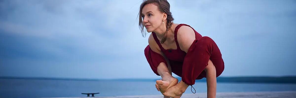 Kobieta ćwicząca na macie w plenerze pozycję bhujapidasana w jodze