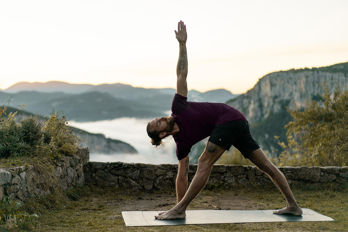 Mężczyzna ćwiczący w plenerze na macie pozycję parivrtta trikonasana w jodze