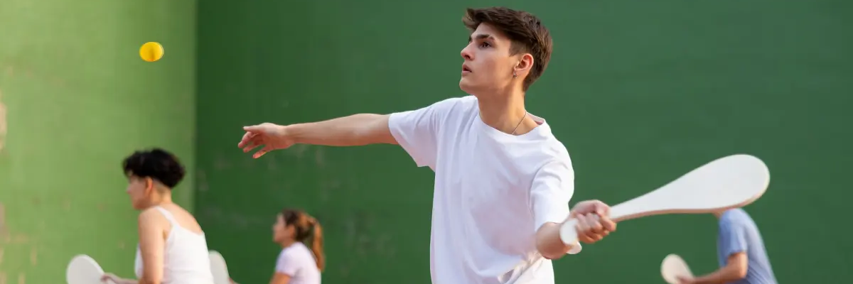 Chłopak w odzieży sportowej grający w pelotę odbijający rakietą piłkę