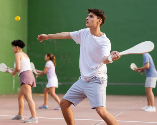 Chłopak w odzieży sportowej grający w pelotę odbijający rakietą piłkę