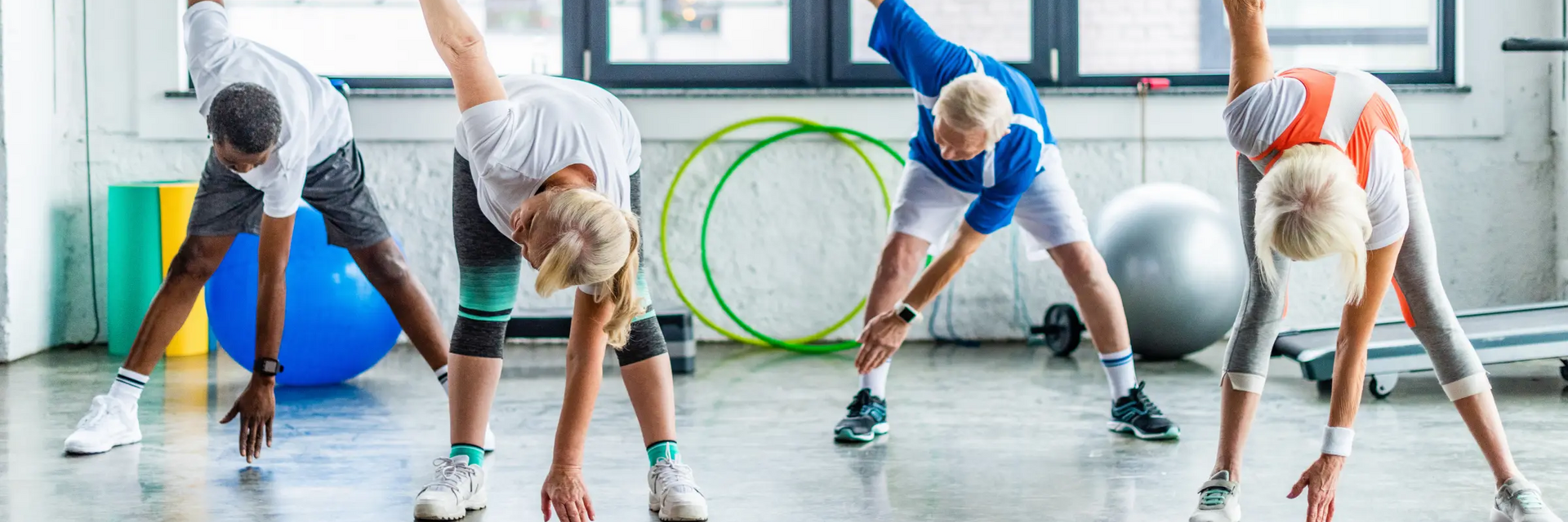 Grupa ludzi w strojach sportowych ćwicząca skrętoskłony na sali gimnastycznej