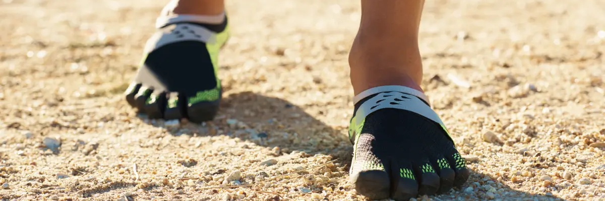 Osoba chodząca po piasku w butach barefoot