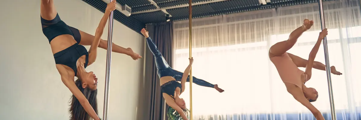 Kobiety w odzieży sportowej ćwiczące figurę butterfly na rurze podczas zajęć pole dance