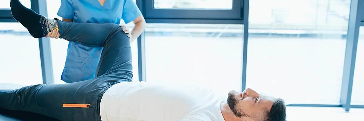 Fizjoterapeutka zginająca nogę mężczyzny leżącego na kozetce