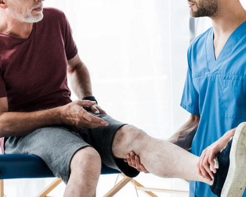 Fizjoterapeuta trzymający wyprostowaną nogę pacjenta siedzącego na kozetce