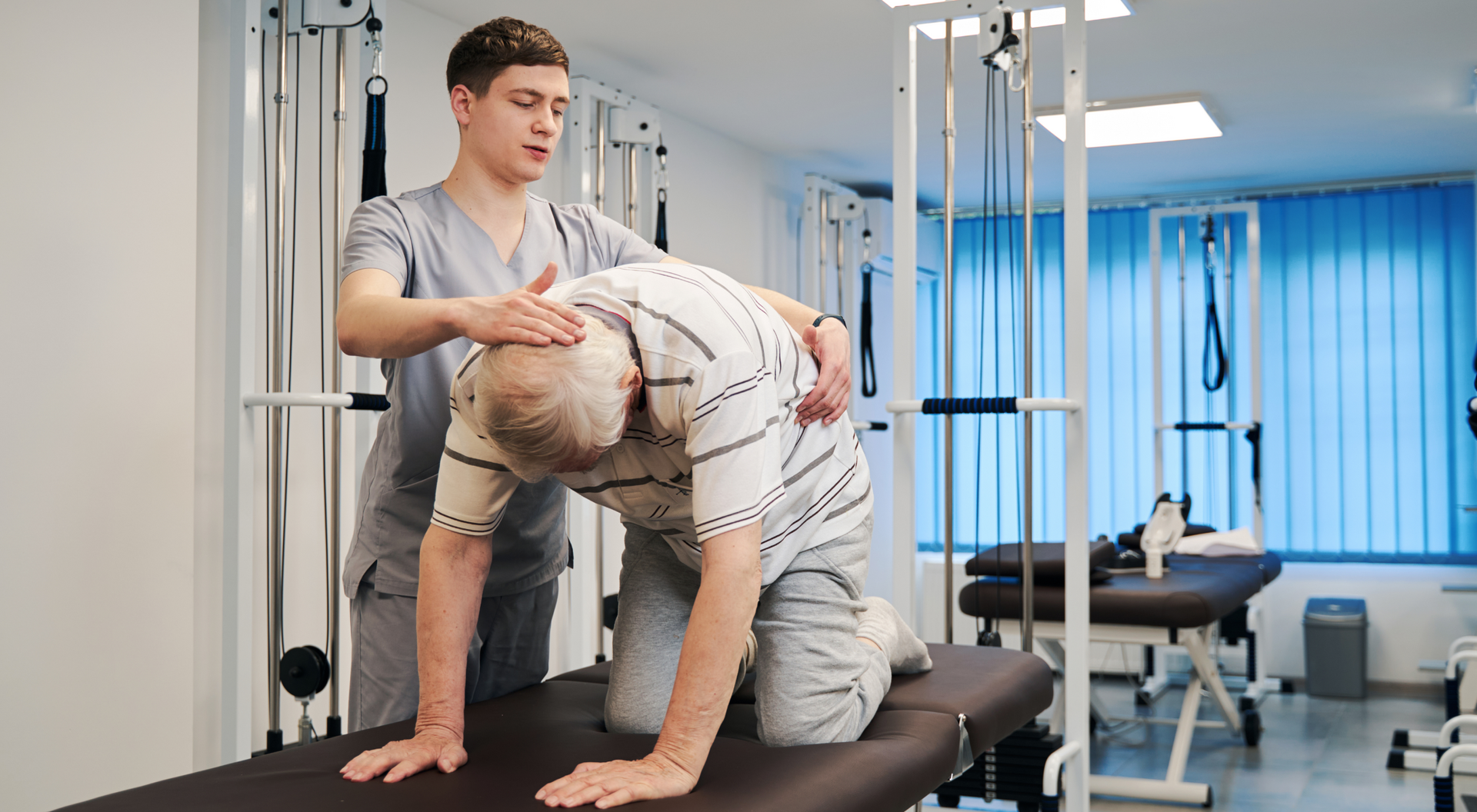 Rehabilitant wykonujący badanie starszemu mężczyźnie w pozycji nastraszonego kota na kozetce