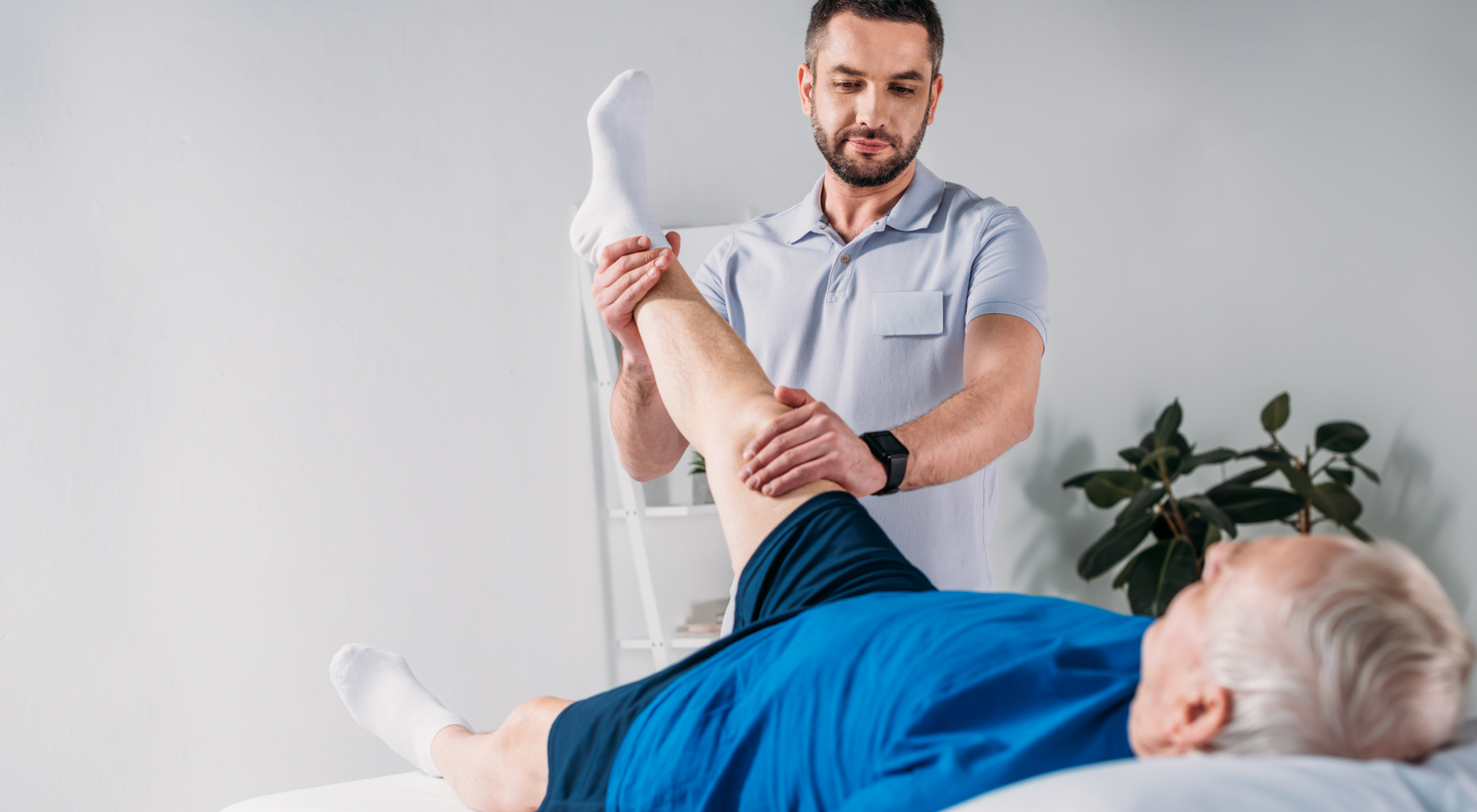 Fizjoterapeuta dotykający wyprostowaną nogę pacjenta leżącego na kozetce