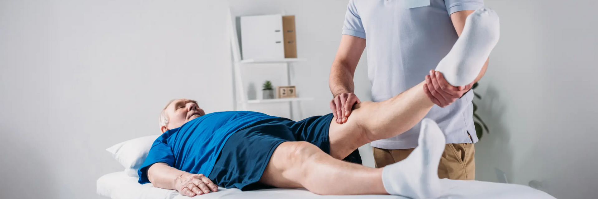 Fizjoterapeuta dotykający kolano w wyprostowanej nodze pacjenta leżącego na kozetce