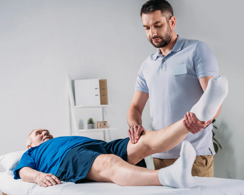 Fizjoterapeuta dotykający kolano w wyprostowanej nodze pacjenta leżącego na kozetce