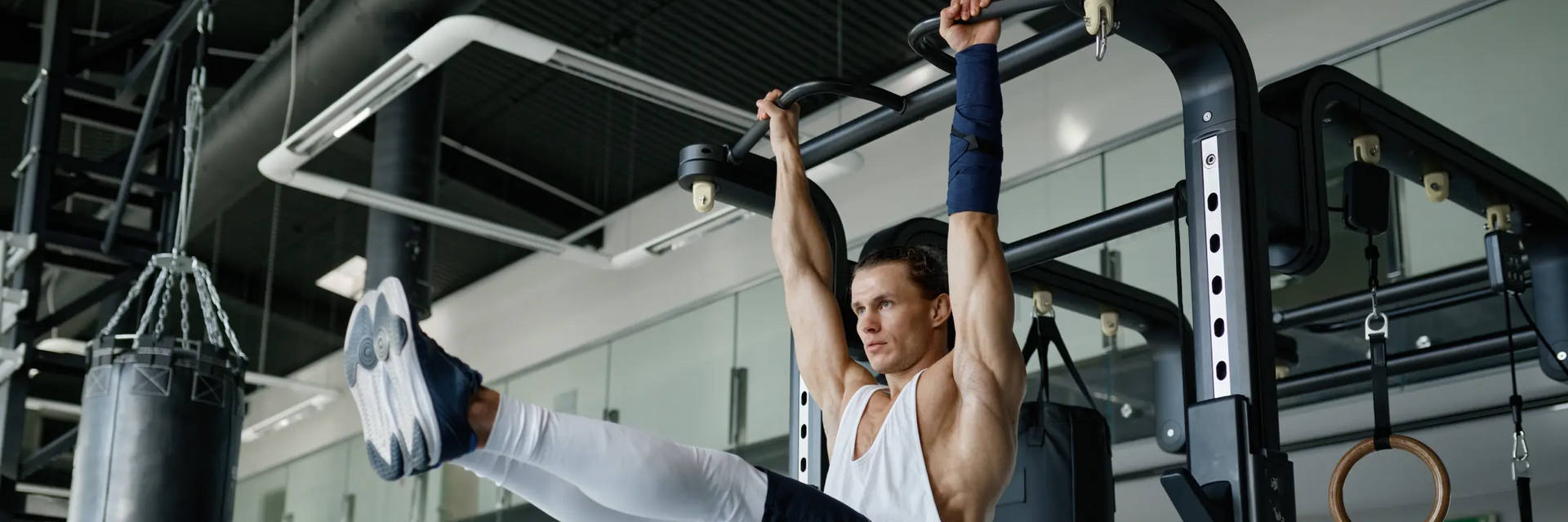 Mężczyzna w odzieży sportowej ćwiczący unoszenie nóg w zwisie na drążku