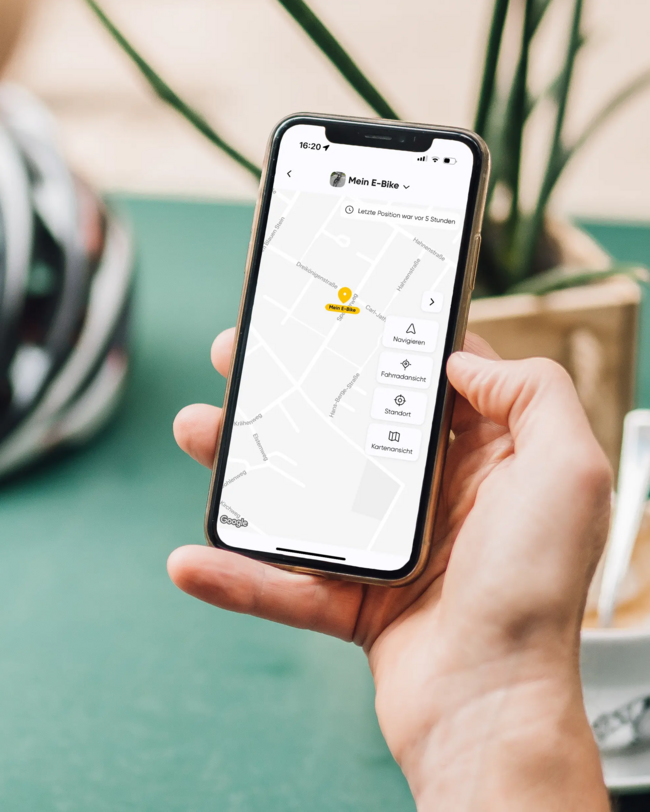 Hand hält Smartphone, auf dem eine Karte mit Trackingfunktion zu sehen ist; im Hintergrund ein Fahrradhelm
