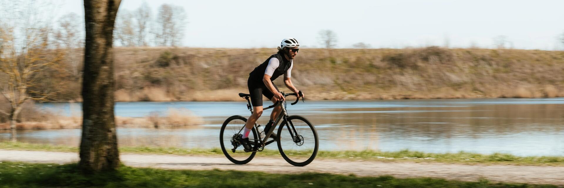 Mężczyzna w kasku i w okularach jadący na rowerze przy jeziorze