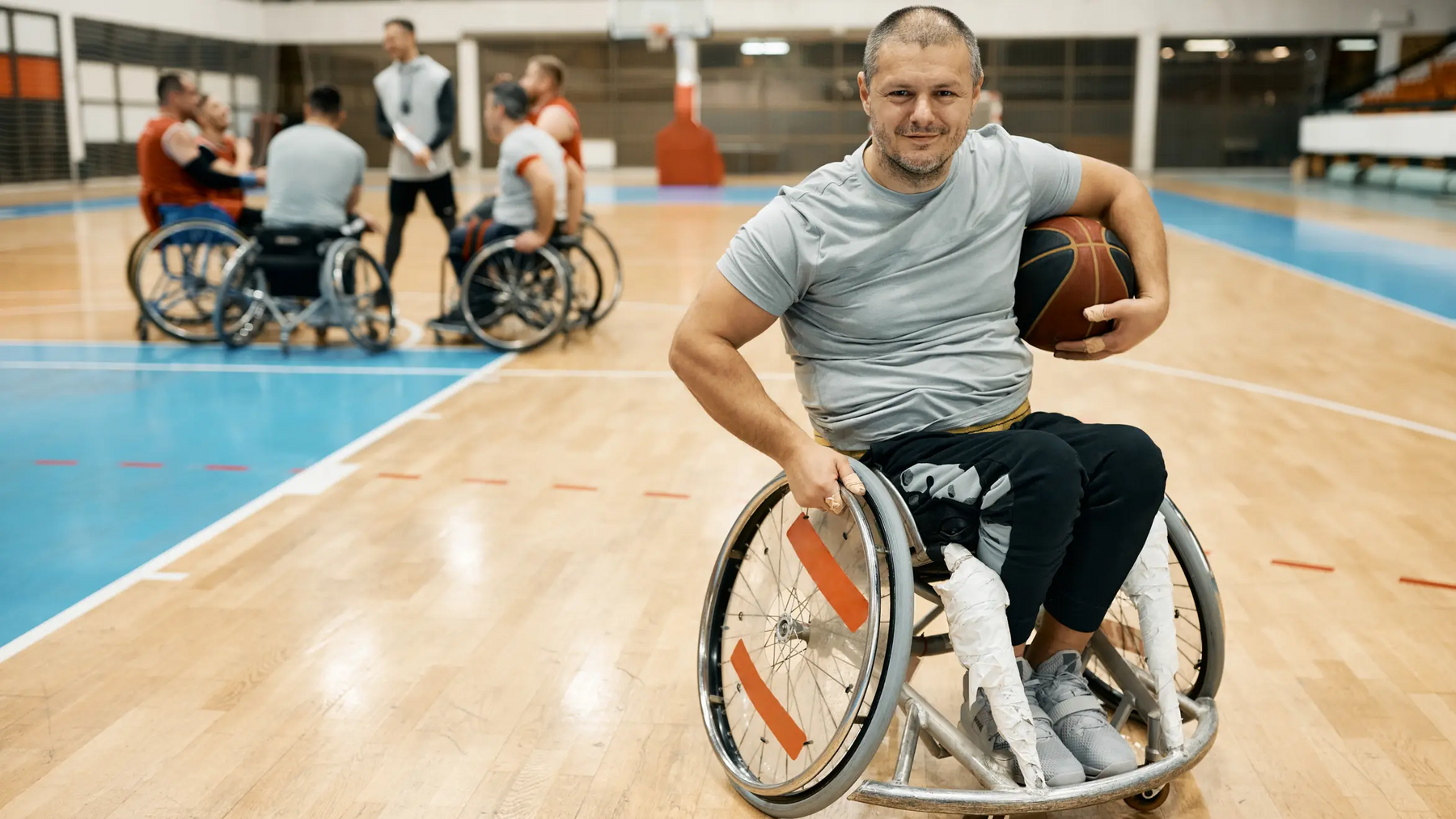 Mężczyzna na wózku trzymający piłkę do koszykówki pod pachą