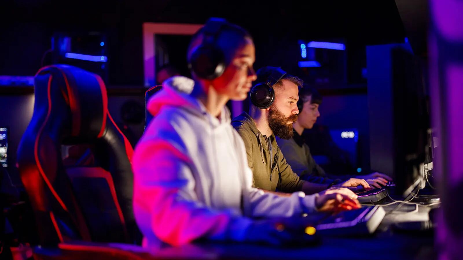 Ludzie w słuchawkach siedzący przed komputerami uprawiający e-sport