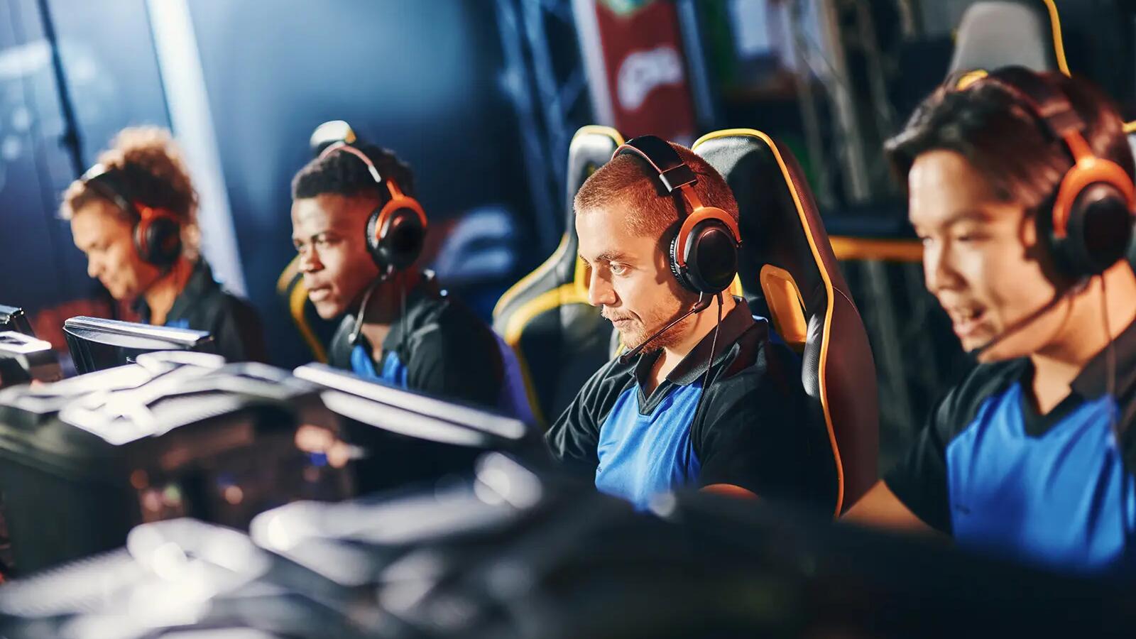 Ludzie w słuchawkach siedzący przed komputerami uprawiający e-sport