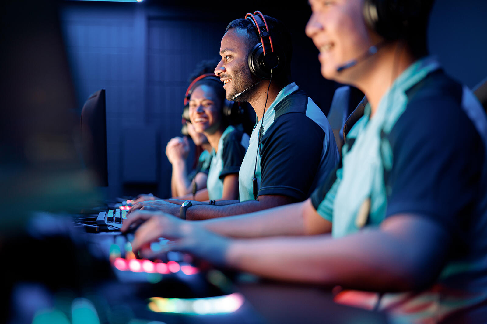 Ludzie w słuchawkach siedzący przed komputerami uprawiający e-sport