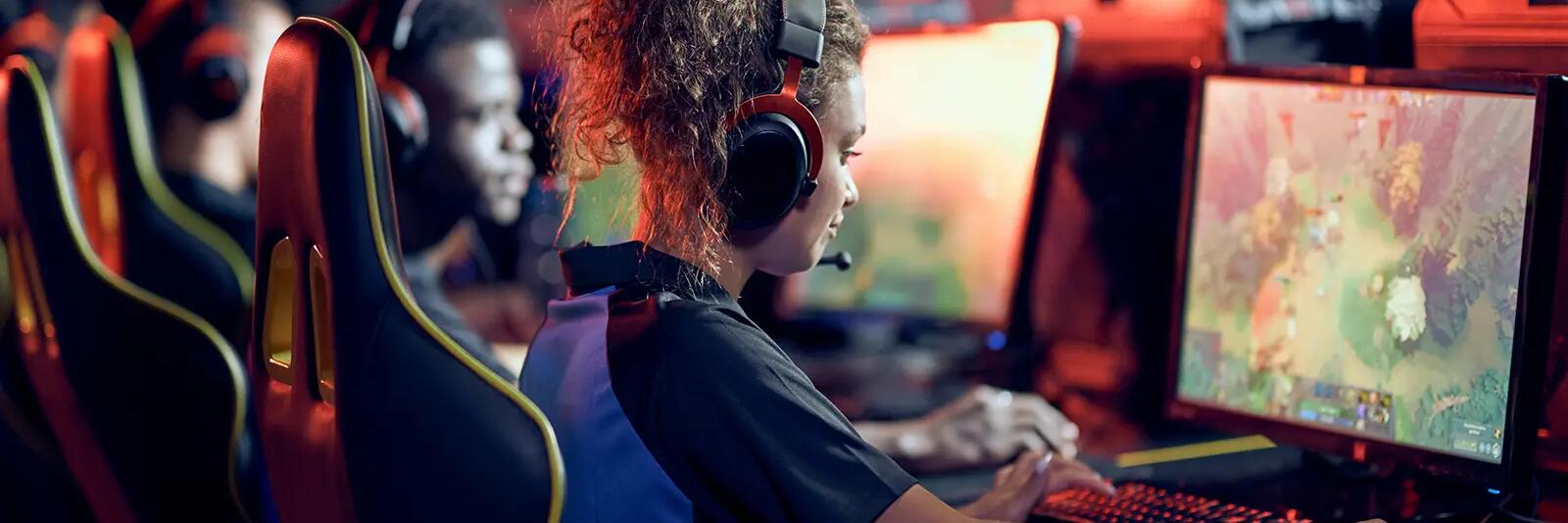 Ludzie w słuchawkach siedzący przed komputerami uprawiający e-sport