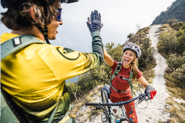Zwei glückliche Mountainbiker geben sich ein High-Five auf einem Bergpfad.