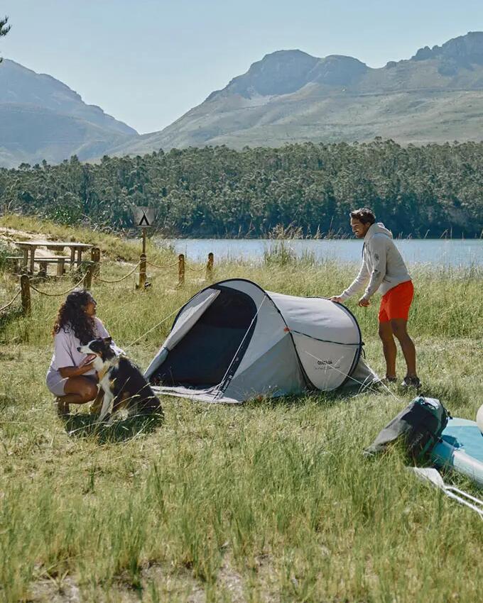 Zwei Personen und ein Hunde campen in der Natur mit einem Quechua-Zelt